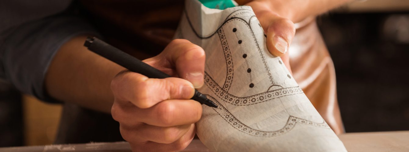 Close up of a male shoemaker drawing design on a new shoes at his workshop
