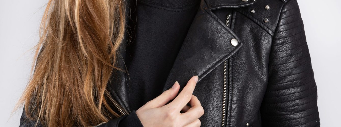 A young female wearing a black jacket standing against a white wall